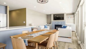A modern kitchen with a central island, a dining area with a wooden table and chairs, and a living area with a sofa and a fireplace.