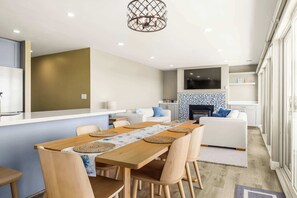 A modern kitchen with a central island, a dining area with a wooden table and chairs, and a living area with a sofa and a fireplace.