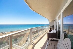 A balcony with a view of the ocean, white chairs, and a wicker sofa.