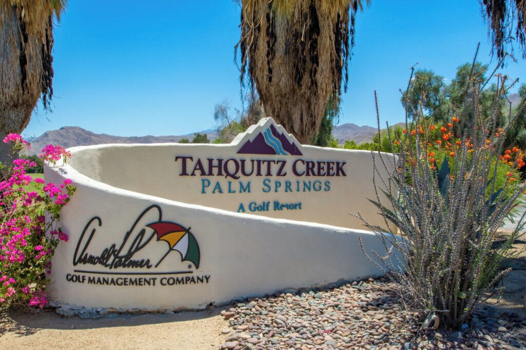 A sign for Tahouitz Creek Palm Springs, a golf resort, with a mountain backdrop and desert flora.