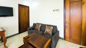 Un salon comprenant un canapé, deux coussins décoratifs, une table basse en bois et deux portes en bois.