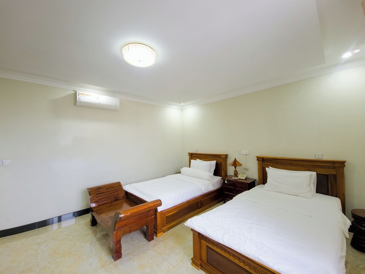 Een slaapkamer met twee houten bedden, een bankje, een nachtkastje en een plafondlamp.