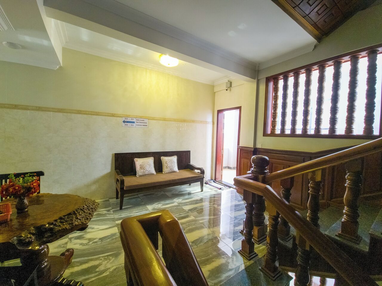 A spacious lobby with a marble floor, a wooden bench, a staircase, and a reception desk.