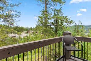 A balcony with a wicker chair, overlooking a forested area with houses in the background. - Snowflake Lift Access | Hot Tub + Views (Breckenridge)