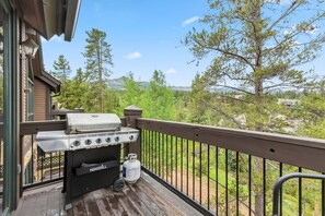 Ein Balkon mit Grill, Propanflasche und Blick auf einen Wald und Berge.