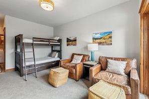 A room with a bunk bed, two leather armchairs, a small table, a lamp, and a woven ottoman.