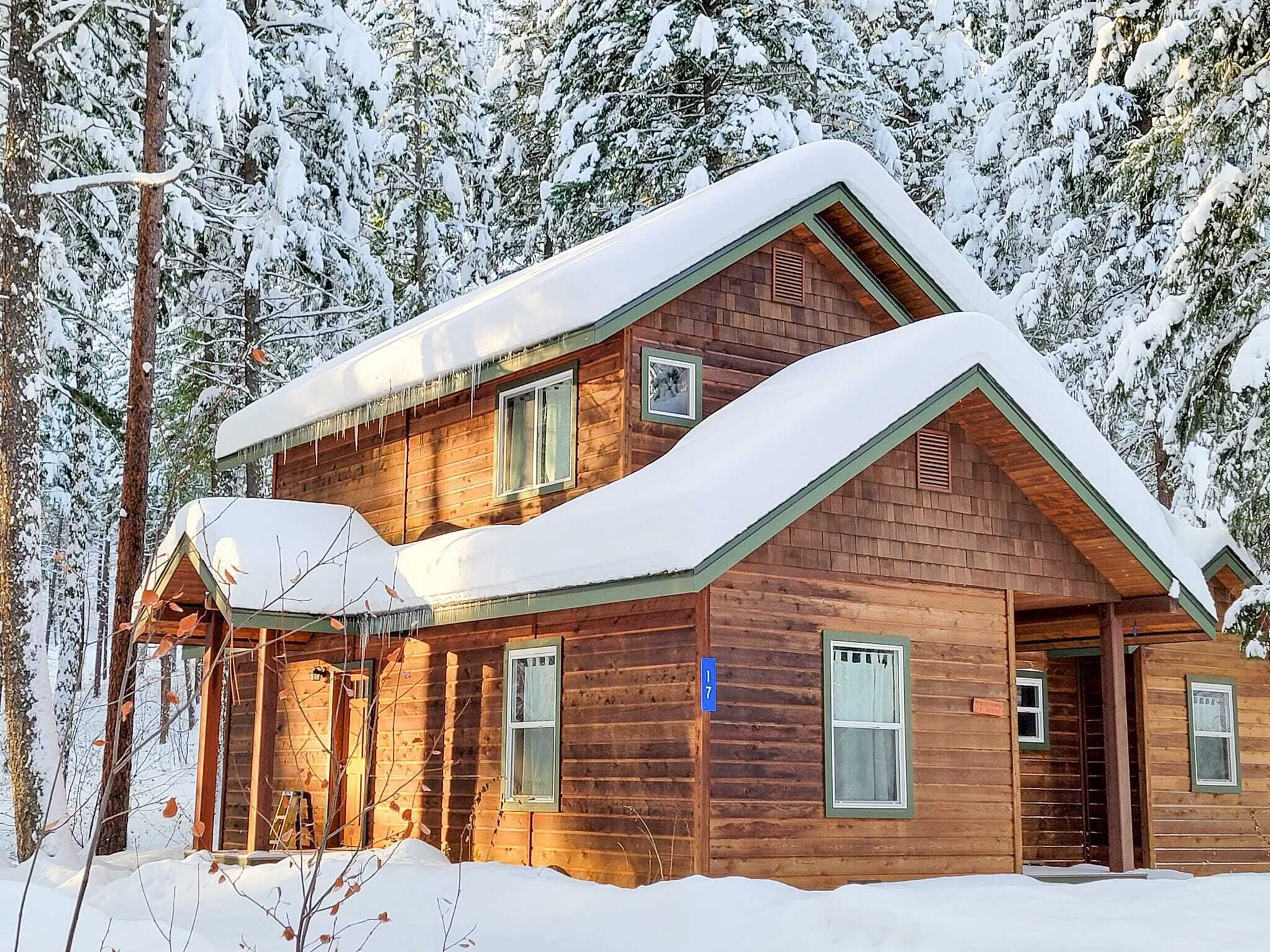 A two-story log cabin with a snow-covered roof, surrounded by trees.