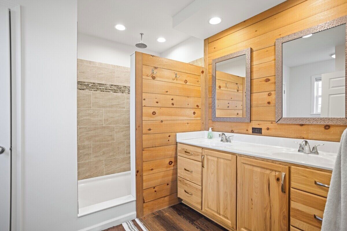 A bathroom with wooden paneling, a bathtub, a large mirror, and a white sink.