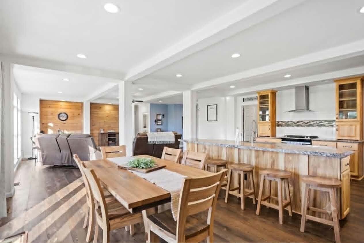 A spacious kitchen with wooden cabinets, a central island with stools, and a dining area with a long wooden table and chairs.