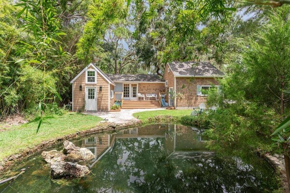 Una casa con un estanque, rodeada de árboles frondosos.