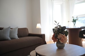A living room with a sofa, a round table with a vase of flowers, and a lamp.