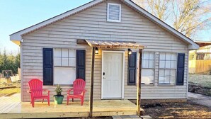 A single-story house with a covered porch, two red Adirondack chairs, and a small potted plant. - Cozy, Country Cottage (Travelers Rest)