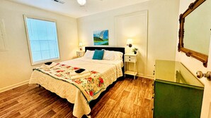 A bedroom with a bed, bedside tables, a nightstand, a ceiling fan, a window with blinds, a painting, and a mirror. - Cozy, Country Cottage (Travelers Rest)
