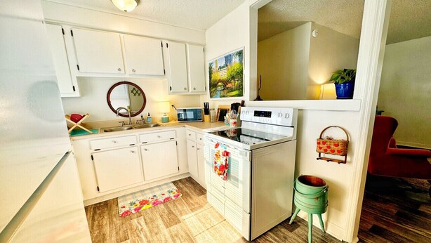 A compact kitchen with white cabinets, a stove, and a microwave. There's a small stool and a green bucket on the floor. - Cozy, Country Cottage (Travelers Rest)