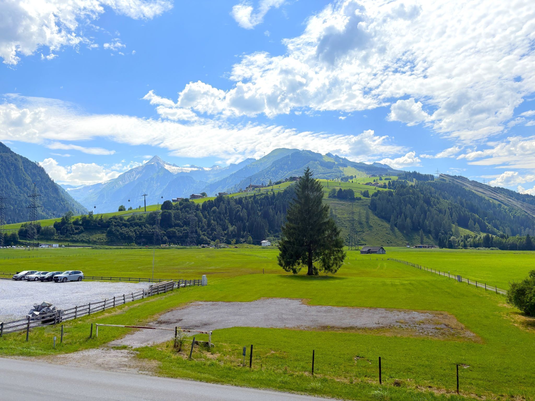 A scenic landscape with mountains, a clear sky, and a fenced field with parked cars.
