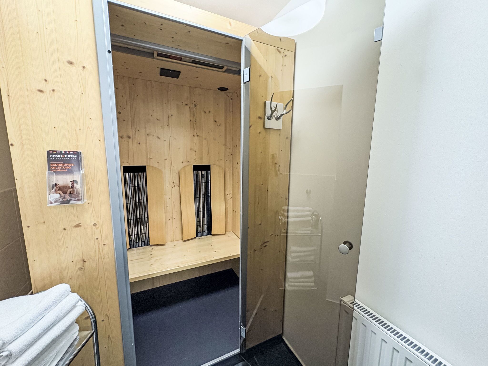 A sauna room with wooden walls and a glass door. There is a poster on the wall and a towel rack with towels.