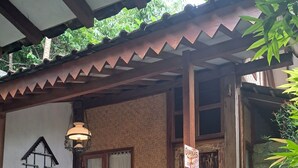 A rustic wooden house with a tiled porch, a hanging lantern, and a small window with a decorative frame. - Diana's Homestay (Banyuwangi)
