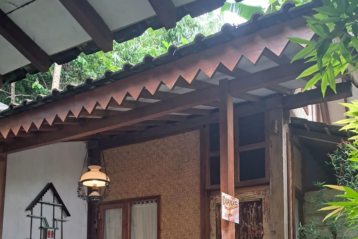 A rustic wooden house with a tiled porch, a hanging lantern, and a small window with a decorative frame.