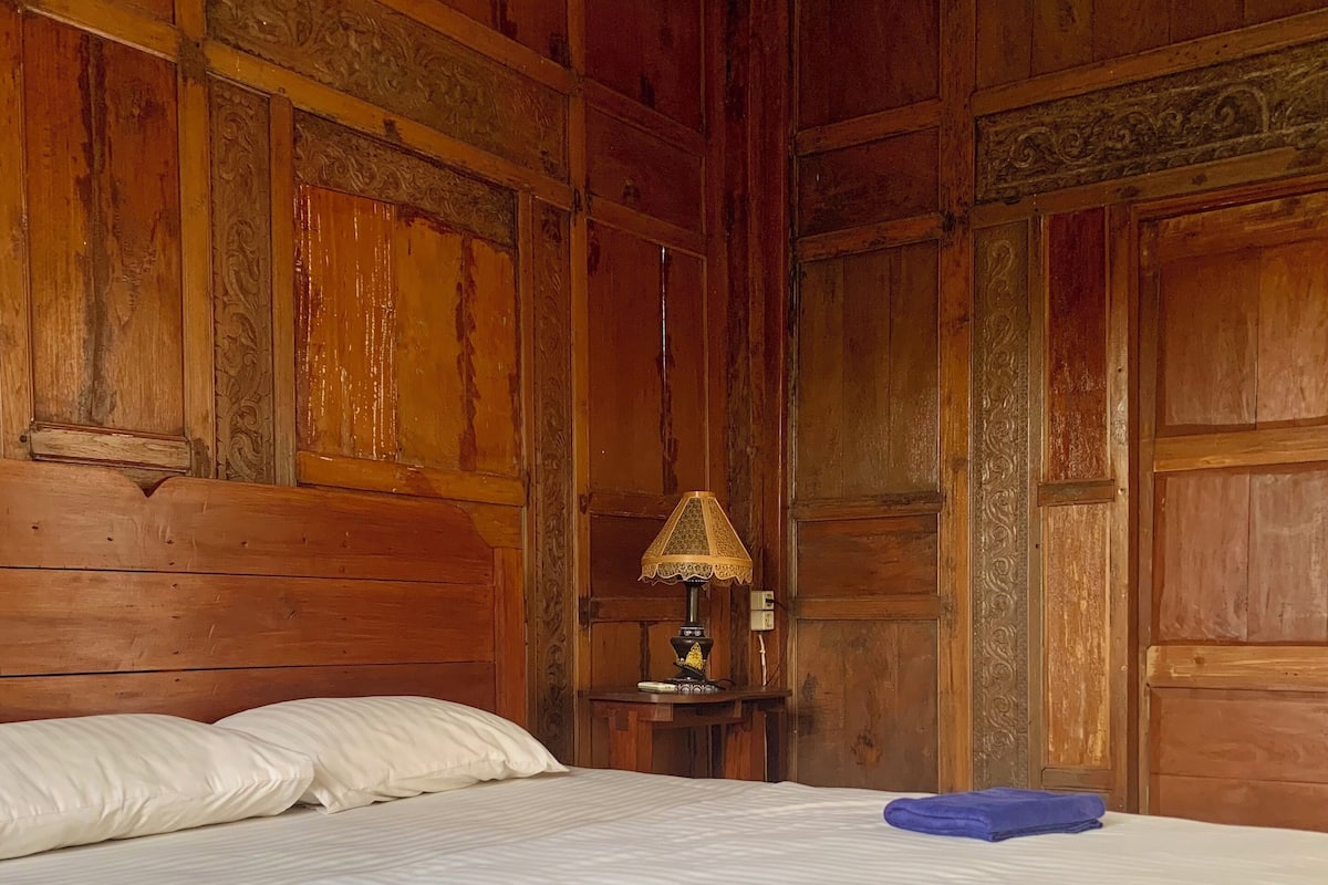 A wooden-paneled room with a bed, a nightstand with a lamp, and a folded towel on the bed.