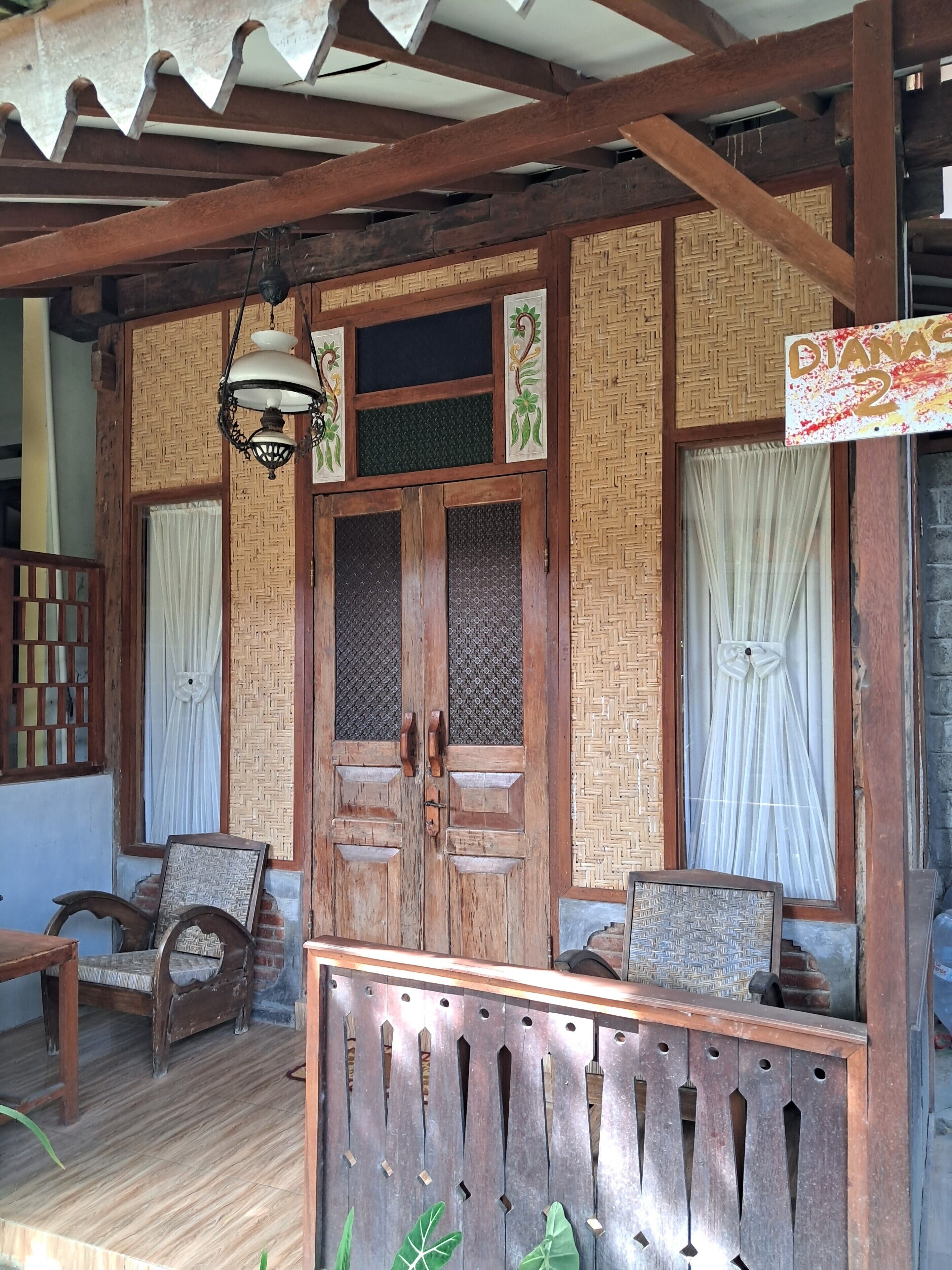 A traditional wooden structure with a covered porch, a large wooden door with decorative panels, and a sign indicating room number 2.