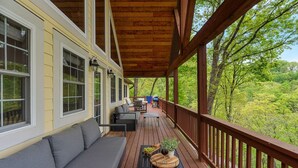 Eine überdachte Veranda mit Holzterrasse, einem grauen Sofa und einem Esstisch mit Blumentopf und Früchten.