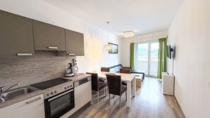 Une cuisine moderne équipée d’une cuisinière, d’un évier et de placards, un coin repas avec une table et des chaises, et une grande fenêtre avec des rideaux.