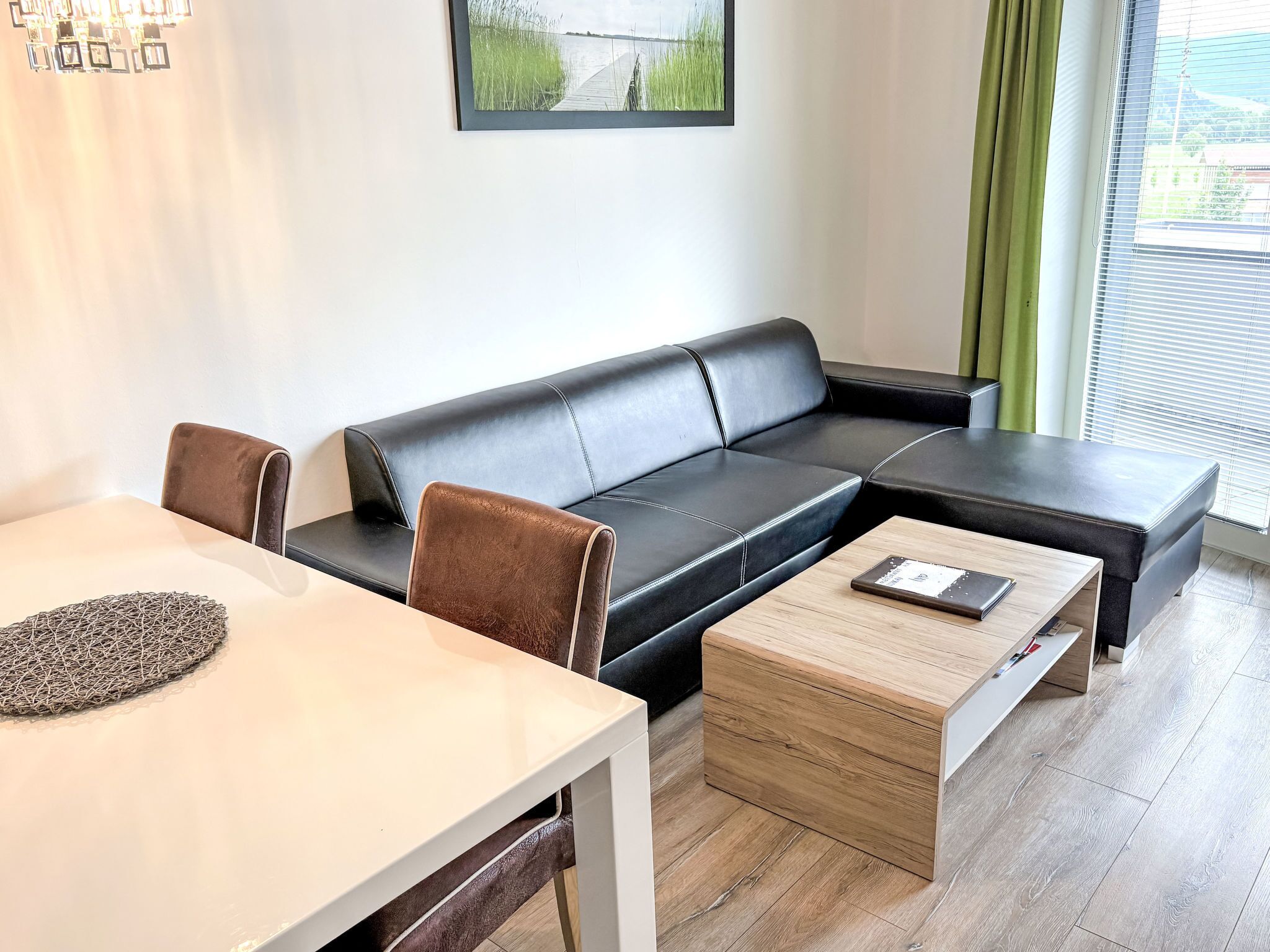 A modern living room with a black leather sofa, a wooden coffee table, and a dining table with a woven placemat.
