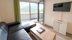Un salon moderne avec un canapé en cuir noir, une table basse en bois et un téléviseur fixé au mur.