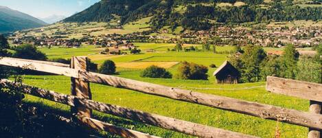 A rural landscape with a wooden fence, a small building, and a village in the valley.