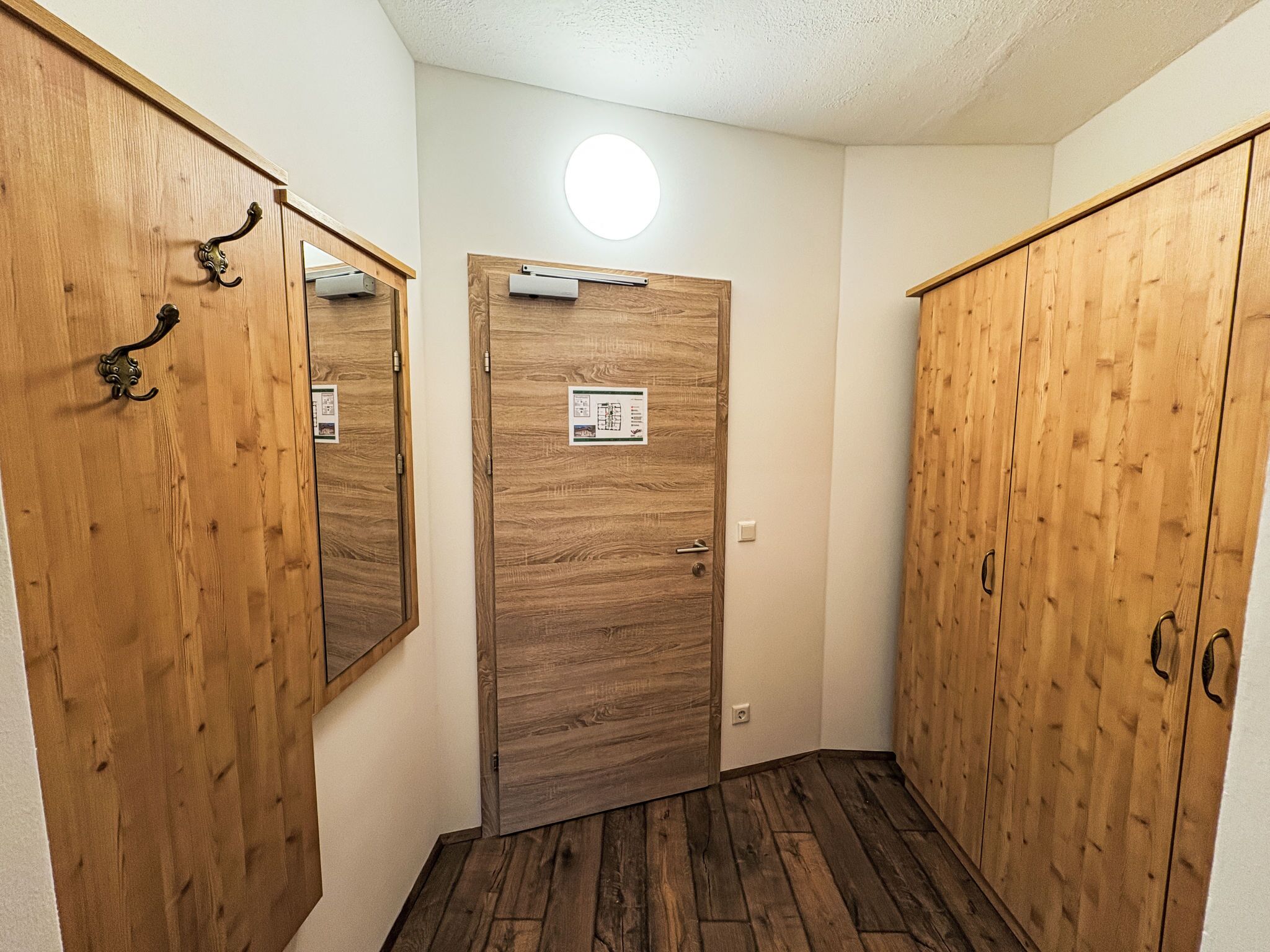 Un pasillo con puertas de madera, un accesorio de iluminación en el techo y un piso con diseño de madera.