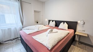 Ein Hotelzimmer mit Bett, Nachttisch, Lampe und einem Fenster mit Vorhängen.