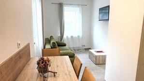 Ein modernes Wohnzimmer mit Esstisch aus Holz, einem grünen Sofa und einem an der Wand befestigten Fernseher.