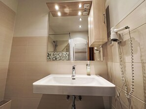 A bathroom with a white sink, a mirror, and a shower. There are lights above the mirror and a towel rack on the wall.
