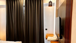 Ein Hotelzimmer mit Bett, Schreibtisch, Stuhl, Fernseher und Vorhang.