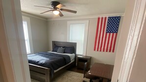 Une chambre à coucher avec un lit, des tables de chevet, un bureau, un ventilateur de plafond et un drapeau américain.
