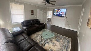 Un salon avec un canapé en cuir, une table basse en verre, un ventilateur de plafond et un téléviseur fixé au mur.