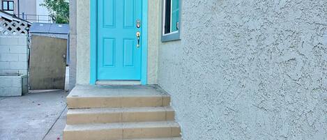 A turquoise door with a small window above it, leading to a concrete staircase.