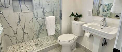 Et moderne badeværelse med en glasafskærmet bruseniche, toilet og håndvask.