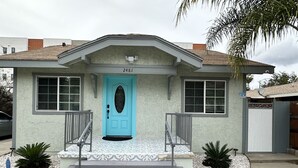 A house with a turquoise door, numbered 2481, and a small porch with steps and railings.