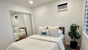 A bedroom with a large bed, a potted plant, a mirror, and a ceiling vent.