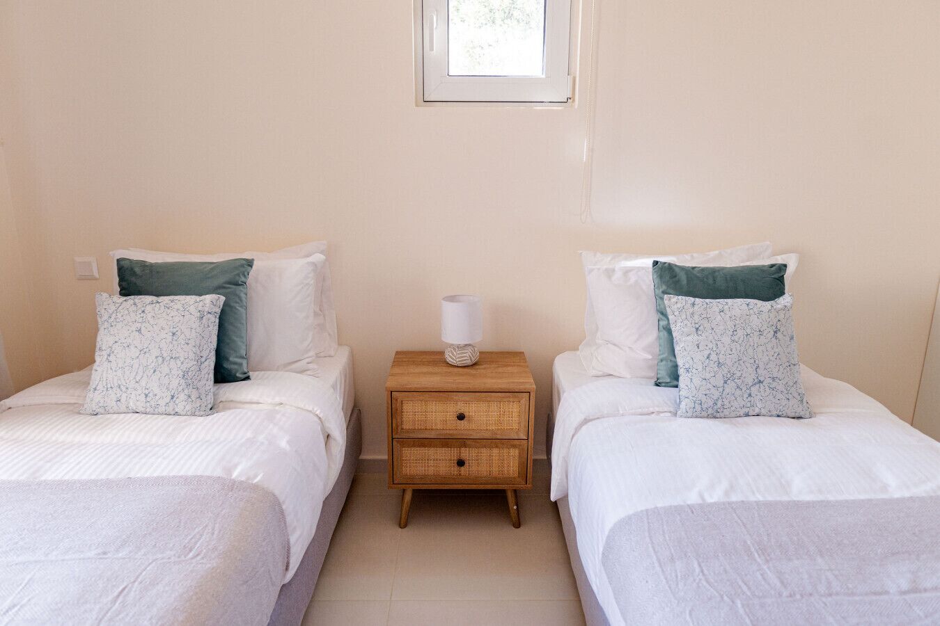 Une chambre à deux lits simples, chaque lit étant équipé d’un oreiller et d’une table de chevet avec une lampe.