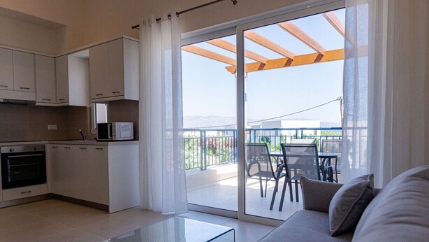 A modern kitchen with white cabinets, a glass coffee table, and a sliding glass door leading to a balcony with outdoor furniture.