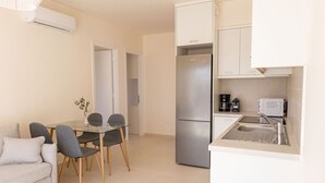 Una cocina compacta equipada con refrigerador, cafetera y pileta. Hay un comedor con mesa de vidrio y sillas.
