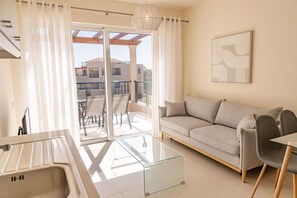 Ein modernes Wohnzimmer mit einer Couch, Sesseln, einem Glastisch und Blick auf den Balkon.