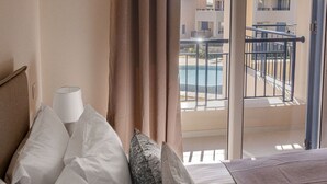 A hotel room with a bed, pillows, a lamp, and a view of a pool and buildings.