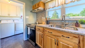 A kitchen with wooden cabinets, a granite countertop, a stainless steel sink, and a window with a view of greenery outside. - Lake Views | King Bed | Fenced (Alpena)