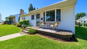A single-story house with a covered porch, a small outdoor seating area, and a well-maintained lawn. - Lake Views | King Bed | Fenced (Alpena)