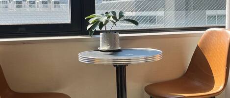 A room with a window overlooking a cityscape, a small round table with a potted plant, and two chairs.