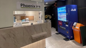 Un comptoir d’accueil d’hôtel avec une enseigne indiquant « Phoenix Inn », un distributeur automatique et une poubelle.
