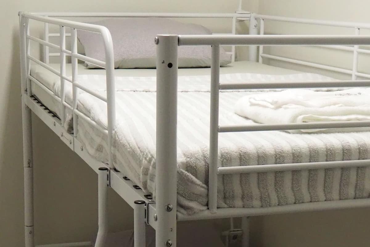 A bunk bed with a mattress and pillows, a metal ladder, and a lower bunk with a patterned blanket.